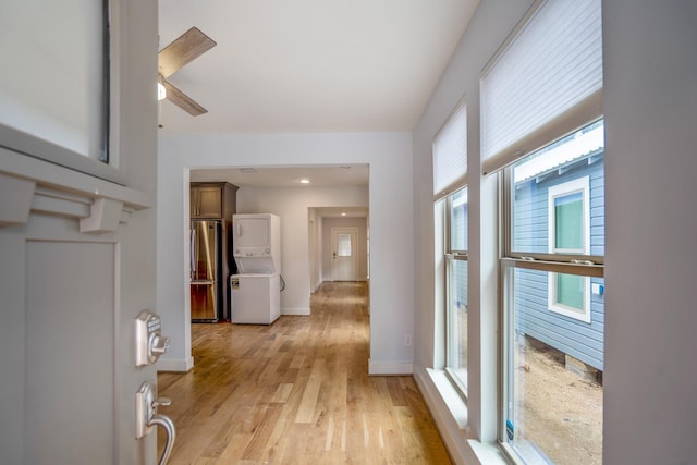 corridor with stacked washer and dryer, light wood-style floors, and baseboards