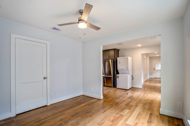 empty room with baseboards, light wood-style floors, visible vents, and stacked washer / drying machine