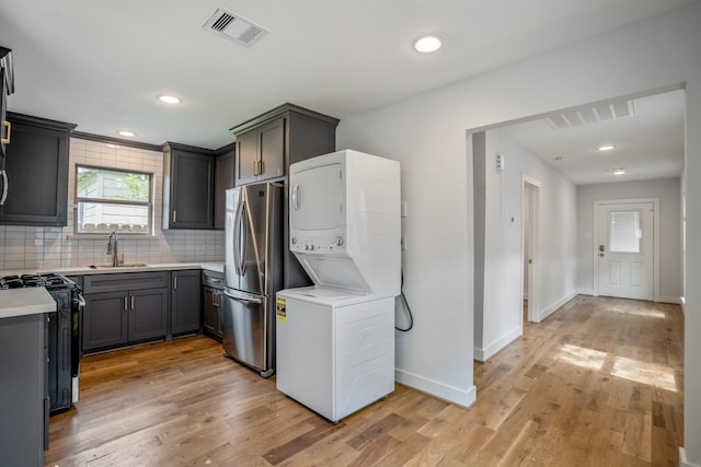 kitchen with visible vents, range with gas cooktop, stacked washer and clothes dryer, freestanding refrigerator, and a sink