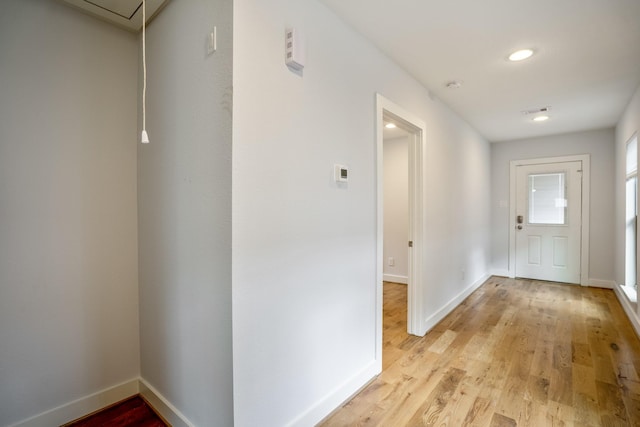 hall with light wood-type flooring, attic access, and baseboards