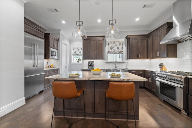 kitchen with built in appliances, dark brown cabinetry, a kitchen island, visible vents, and wall chimney range hood