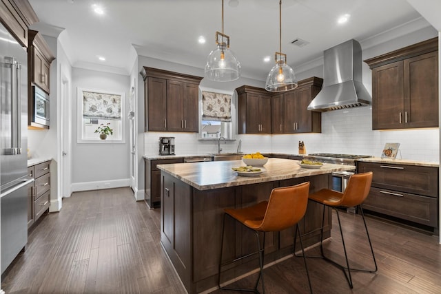 kitchen with wall chimney exhaust hood, a center island, stainless steel appliances, dark brown cabinets, and a sink