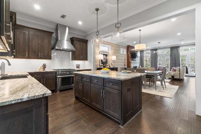 kitchen featuring light stone counters, dark brown cabinetry, a sink, high end stove, and wall chimney exhaust hood