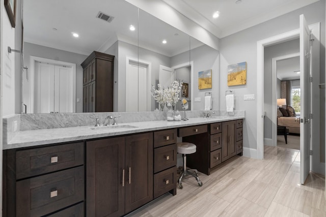 ensuite bathroom with a sink, visible vents, baseboards, double vanity, and crown molding