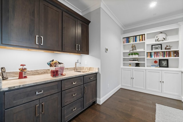 kitchen featuring dark brown cabinetry, dark wood-style floors, ornamental molding, light stone countertops, and a sink