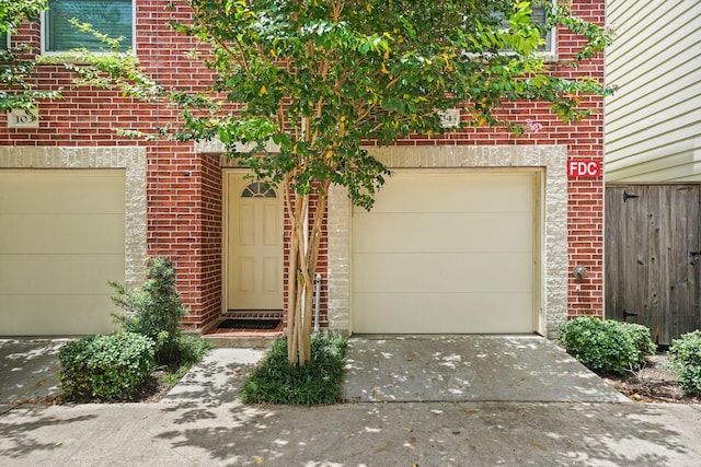 doorway to property with a garage, brick siding, and driveway