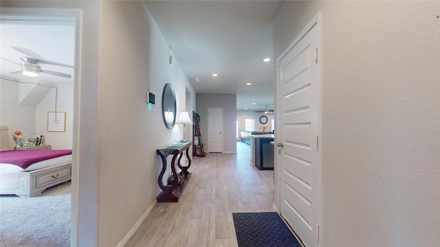 hallway featuring baseboards, light wood finished floors, and recessed lighting