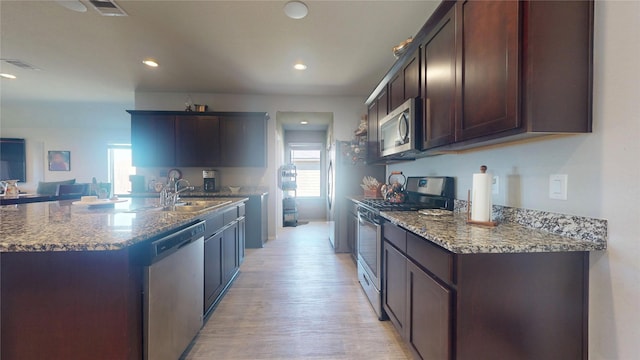 kitchen featuring light wood finished floors, visible vents, a sink, dark stone counters, and appliances with stainless steel finishes