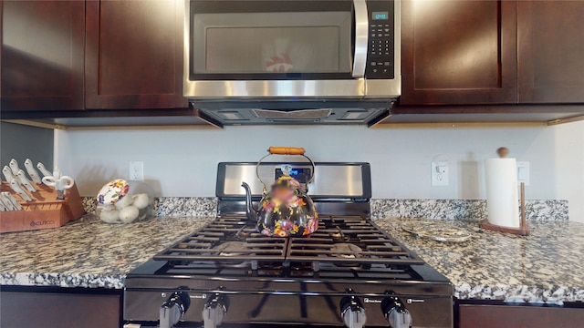 kitchen with stainless steel microwave, stone countertops, gas range, and dark brown cabinetry