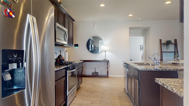 kitchen with dark brown cabinetry, stone counters, appliances with stainless steel finishes, and a sink