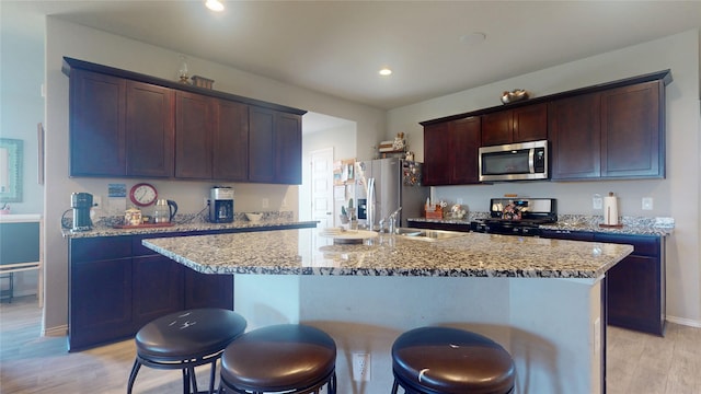 kitchen featuring light wood finished floors, a center island with sink, a kitchen breakfast bar, stainless steel appliances, and a sink