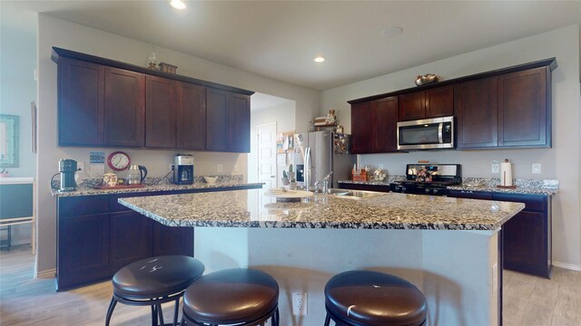 kitchen featuring a sink, recessed lighting, light wood-style flooring, a kitchen bar, and appliances with stainless steel finishes