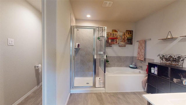 full bath featuring a stall shower, recessed lighting, a bath, and wood finished floors