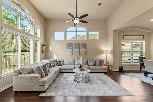 living area featuring ceiling fan, a high ceiling, visible vents, baseboards, and dark wood finished floors