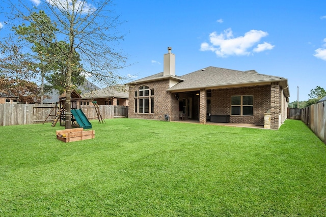 back of property with a fenced backyard, brick siding, a lawn, a chimney, and a patio area