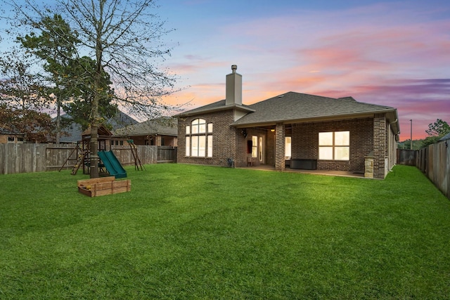 back of house featuring a playground, a fenced backyard, brick siding, a lawn, and a chimney