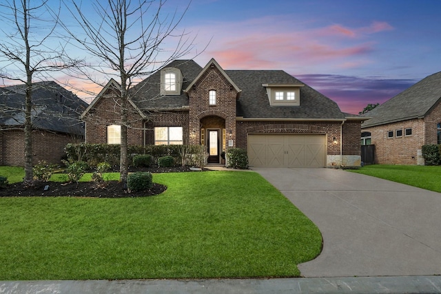 view of front of home featuring driveway, a shingled roof, an attached garage, a yard, and brick siding