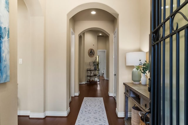 corridor featuring arched walkways, baseboards, and wood finished floors