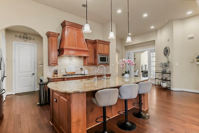 kitchen with arched walkways, light stone counters, a sink, appliances with stainless steel finishes, and custom range hood