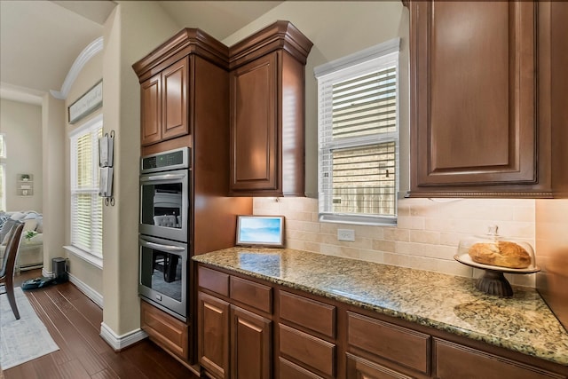 kitchen featuring light stone counters, stainless steel double oven, backsplash, and a wealth of natural light