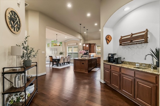 kitchen featuring an island with sink, dark wood-style floors, decorative light fixtures, light stone countertops, and a sink