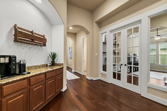 bar featuring arched walkways, dark wood finished floors, baseboards, ceiling fan, and a sink