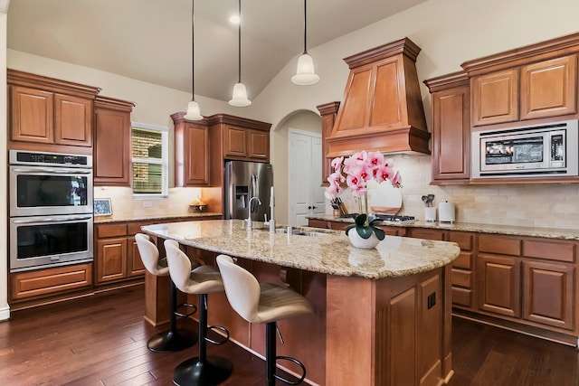 kitchen with an island with sink, lofted ceiling, stainless steel appliances, premium range hood, and a sink