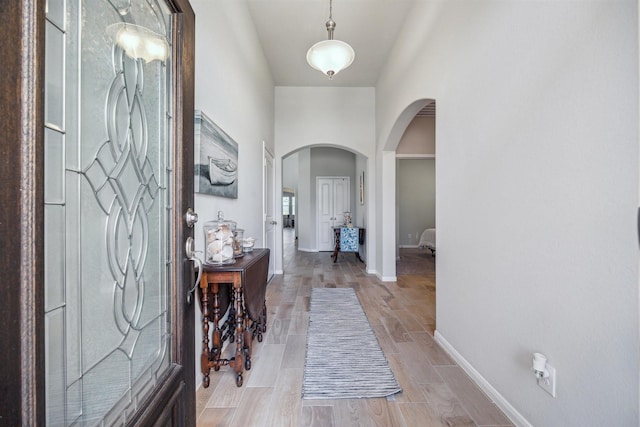 foyer featuring wood tiled floor, arched walkways, and baseboards