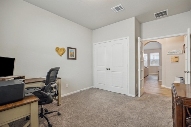 carpeted home office featuring baseboards, visible vents, and arched walkways