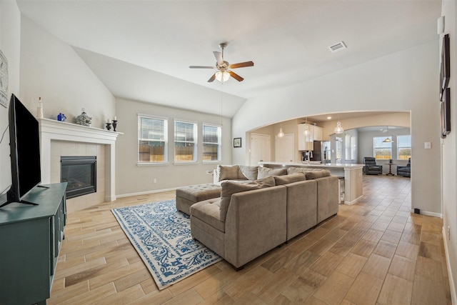 living room with arched walkways, a tiled fireplace, lofted ceiling, ceiling fan, and wood tiled floor