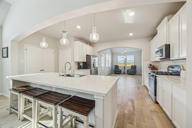 kitchen featuring decorative backsplash, arched walkways, stainless steel appliances, and a sink