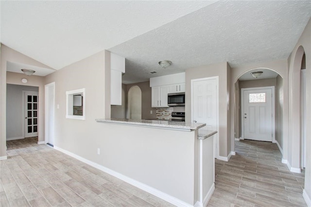 kitchen featuring arched walkways, white cabinets, light stone counters, appliances with stainless steel finishes, and wood tiled floor