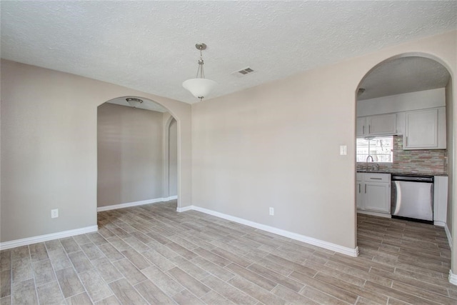 unfurnished room featuring wood finish floors, a sink, arched walkways, and baseboards