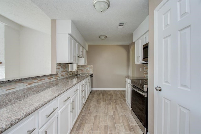 kitchen featuring light stone counters, stainless steel appliances, backsplash, white cabinets, and a sink