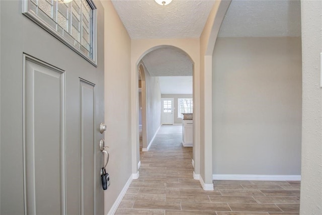 foyer featuring arched walkways, a textured ceiling, baseboards, and wood tiled floor