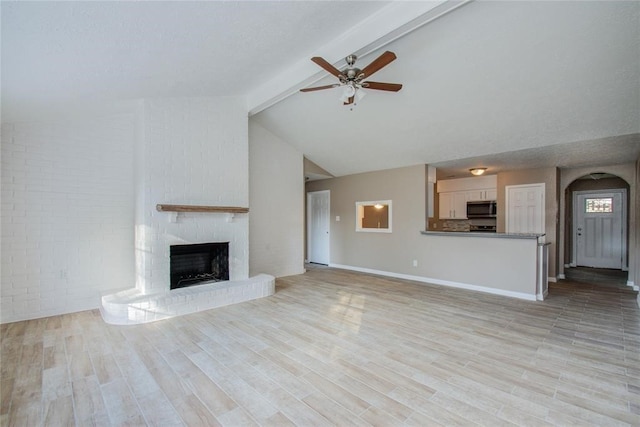 unfurnished living room with vaulted ceiling with beams, a fireplace, light wood finished floors, ceiling fan, and baseboards