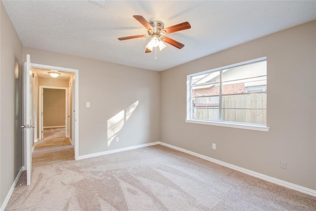 spare room featuring attic access, light carpet, ceiling fan, a textured ceiling, and baseboards