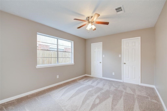 spare room featuring light colored carpet, visible vents, ceiling fan, and baseboards