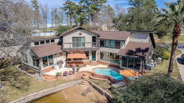 rear view of house featuring a balcony, stone siding, roof with shingles, a patio area, and central AC