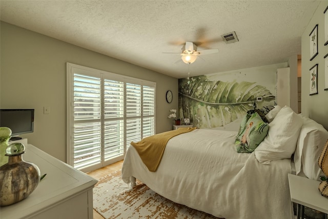 bedroom with light wood finished floors, ceiling fan, visible vents, and a textured ceiling