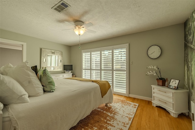 bedroom with light wood-style floors, visible vents, a textured ceiling, and a ceiling fan