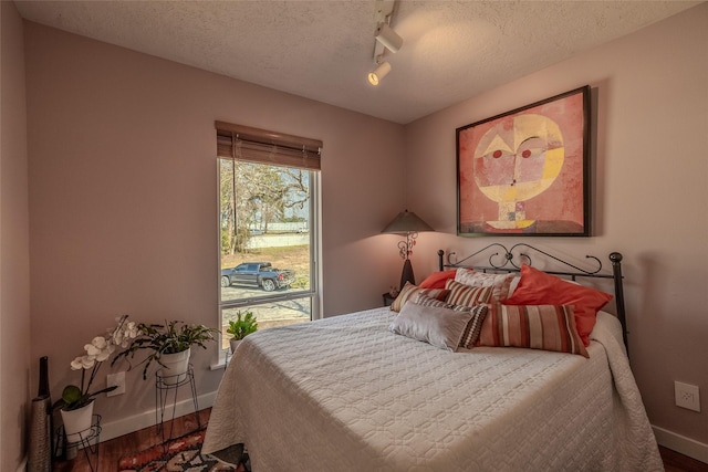 bedroom featuring a textured ceiling, baseboards, track lighting, and wood finished floors