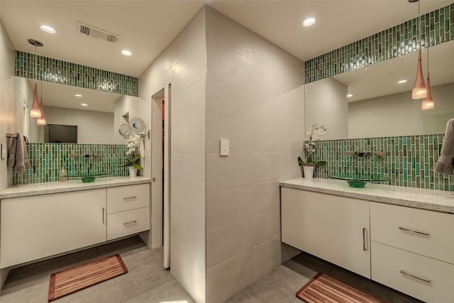 full bath featuring recessed lighting, two vanities, visible vents, a sink, and tile walls