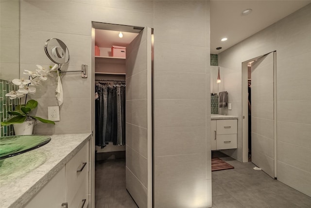 bathroom with tile walls, tile patterned flooring, vanity, and a spacious closet