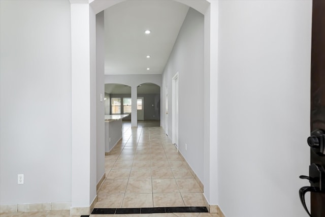 hall with arched walkways, baseboards, recessed lighting, and light tile patterned floors