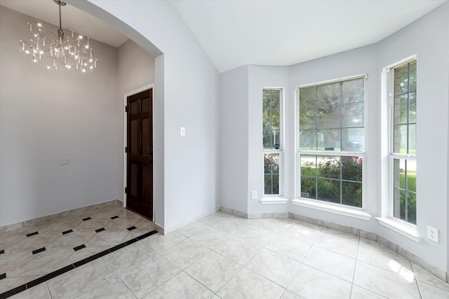 tiled entryway featuring arched walkways, a healthy amount of sunlight, lofted ceiling, and an inviting chandelier