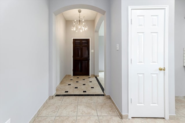 foyer entrance with light tile patterned floors, baseboards, arched walkways, and a notable chandelier