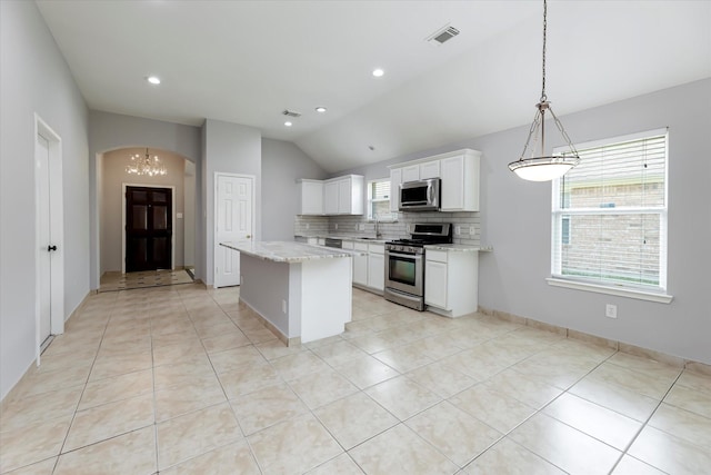 kitchen featuring arched walkways, a kitchen island, visible vents, appliances with stainless steel finishes, and tasteful backsplash