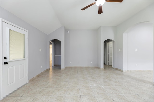 empty room with a ceiling fan, arched walkways, light tile patterned flooring, and baseboards