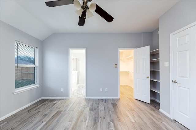 unfurnished bedroom with light wood-style flooring, a spacious closet, baseboards, and vaulted ceiling